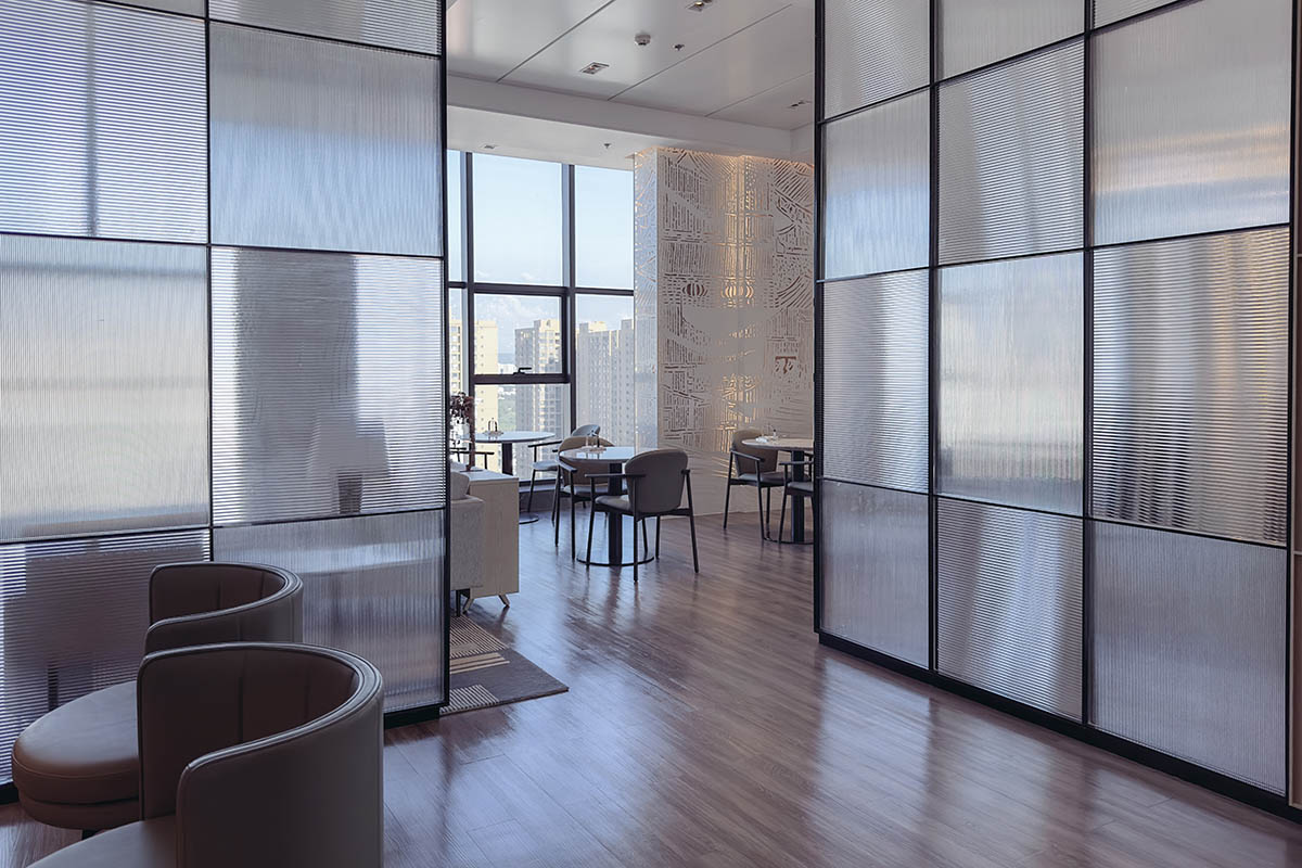 Modern office interior with a sleek, minimalist design. The space includes a long, white marble desk with two comfortable gray chairs and computer workstations. A partition made of large glass panels
